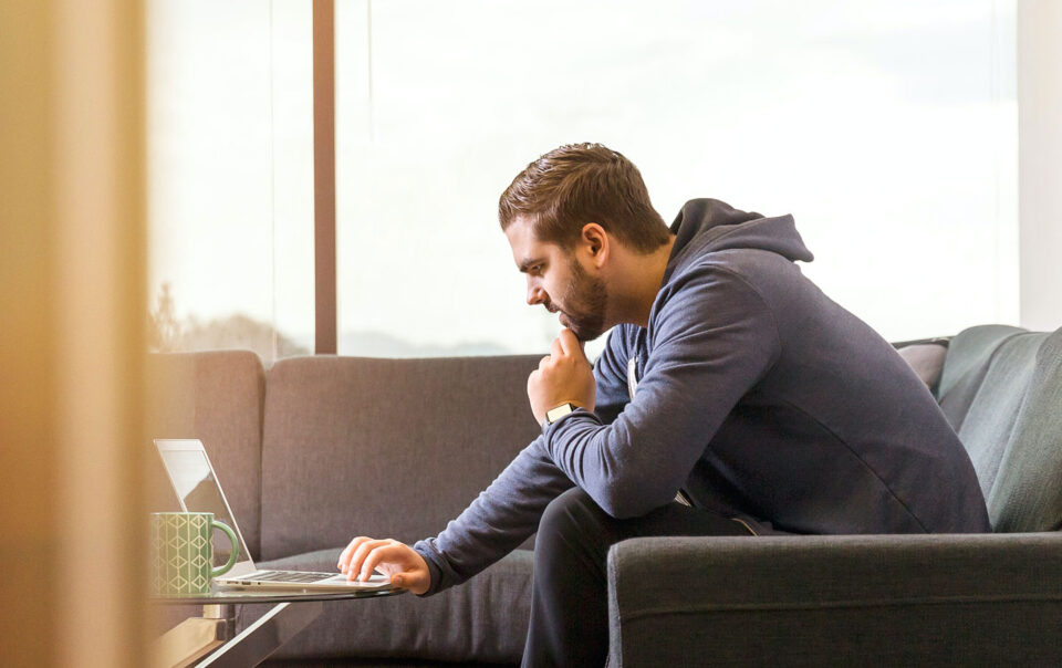 Man sitting on couch looking at his laptop computer.