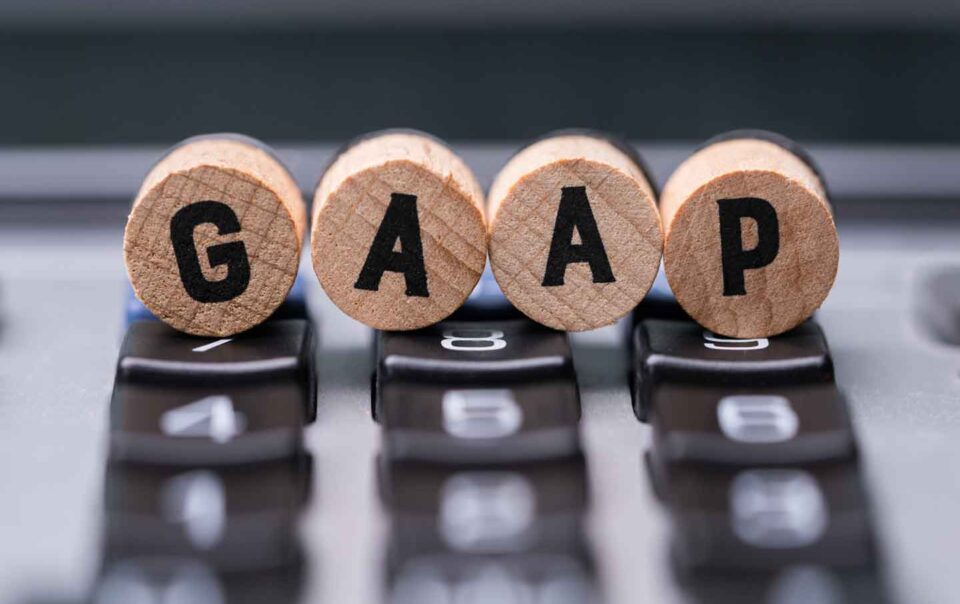 Round wooden dowels with the letters GAAP on the front of them resting on a calculator.