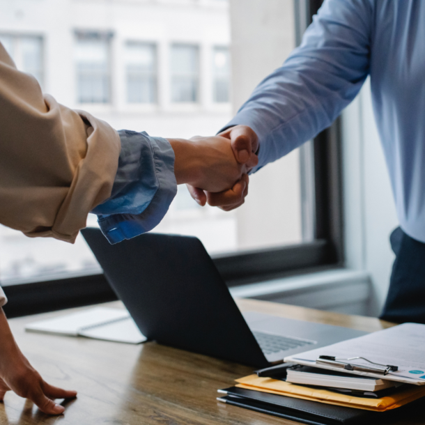 Two Caucasian people shaking hands over a desk.