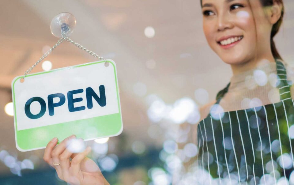 Asian woman business owner holding open sign