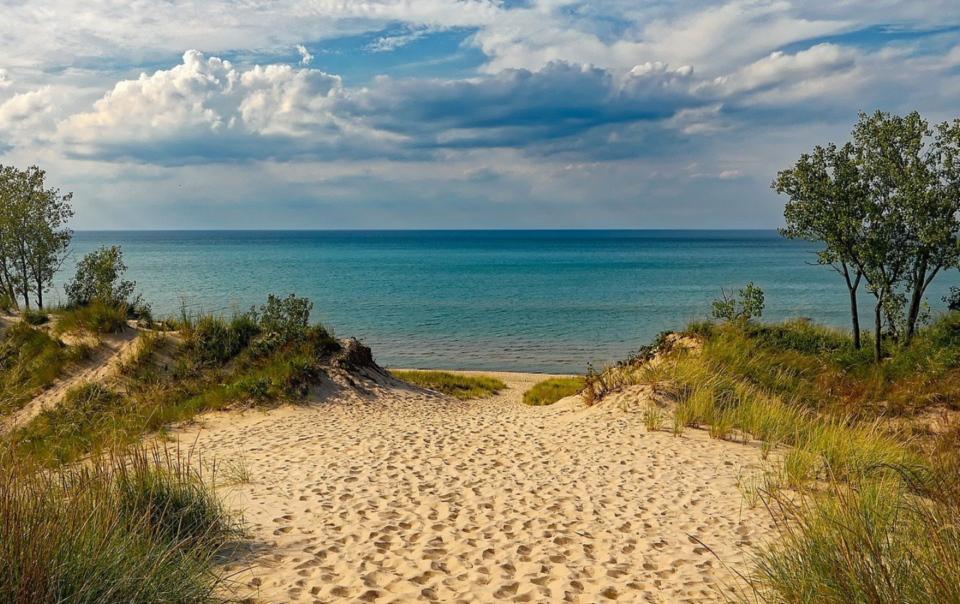 A sandy beach path to water with a blue sky and clouds.