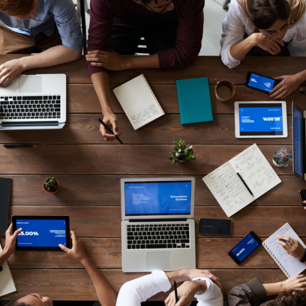 Coworkers sitting around a table with laptops, tablets and paperwork all over the table.