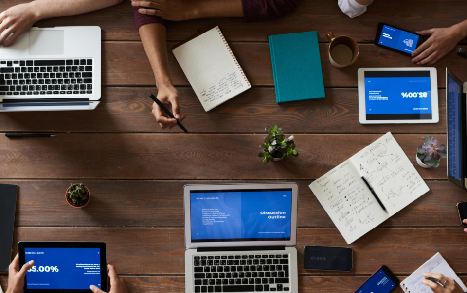 Coworkers sitting around a table with laptops, tablets and paperwork all over the table.