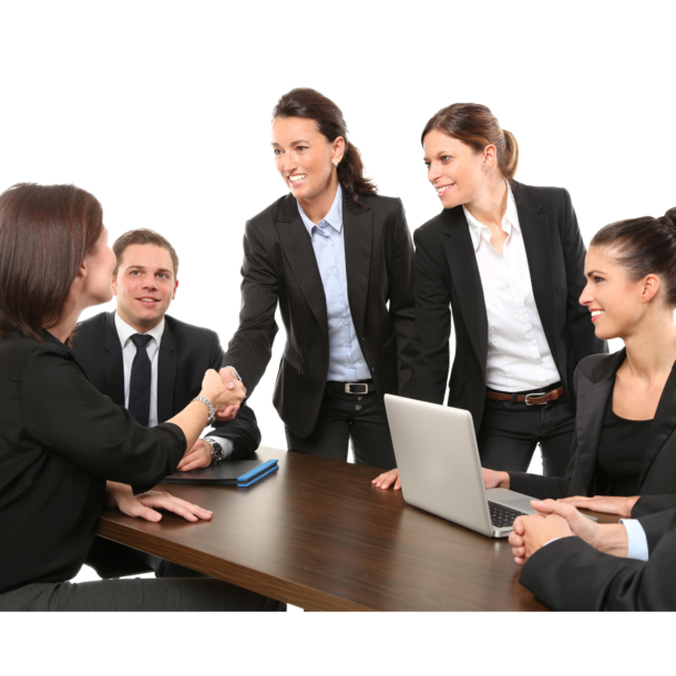 Five colleagues dressed in suits, two are shaking hands, one is on a laptop. They are all sitting at a big wooden table.
