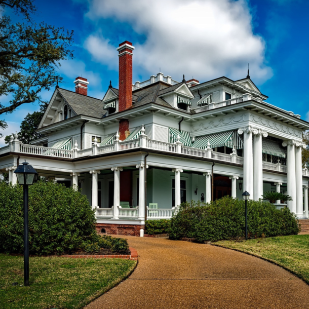 Large white regal mansion with meticulous lawn and sunny blue sky.
