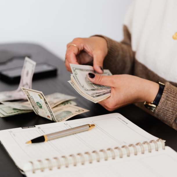 Two hands counting money next to an open notebook.