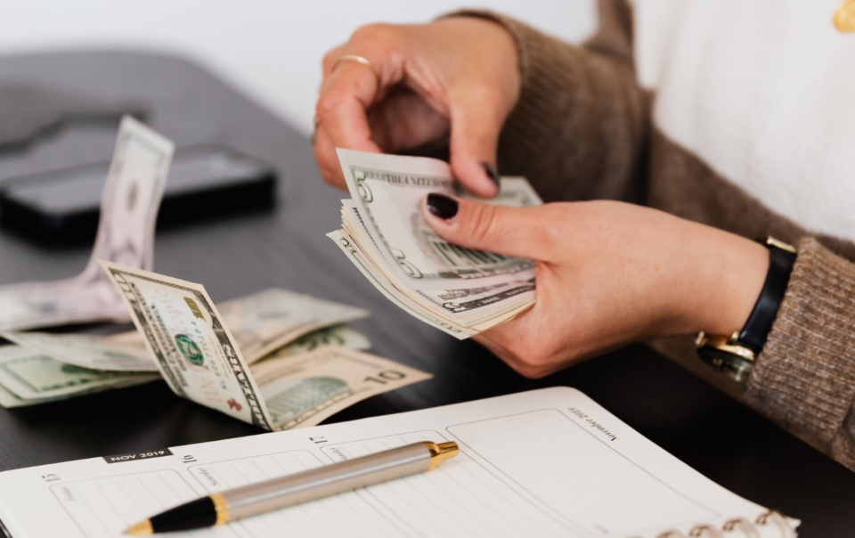 Two hands counting money next to an open notebook.